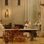 Derrière l'autel, la communauté chante l'office en présence du Christ. Un grand bouquet de feuillages d'automne orne l'autel.