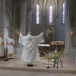 Fr Comlomban les bras levés devant l'autel
