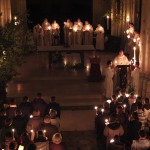 Dans la grande église, illuminée seulement par les cierges et vue depuis la tribune de l'orgue, un prêtre chante l'Exultet à l'ambon, sur la gauche. La communauté se trouve au fond, et les autres fidèles par devant. Le cierge pascal, sur la gauche se trouve dans un arbre fleuri et illuminé. Devant l'autel, la cuve baptismale est prête pour le rite de l'eau.