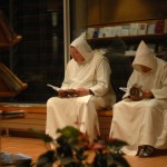 Deux moines, capuchons en tête, sont côte à côte et lisent des revues.