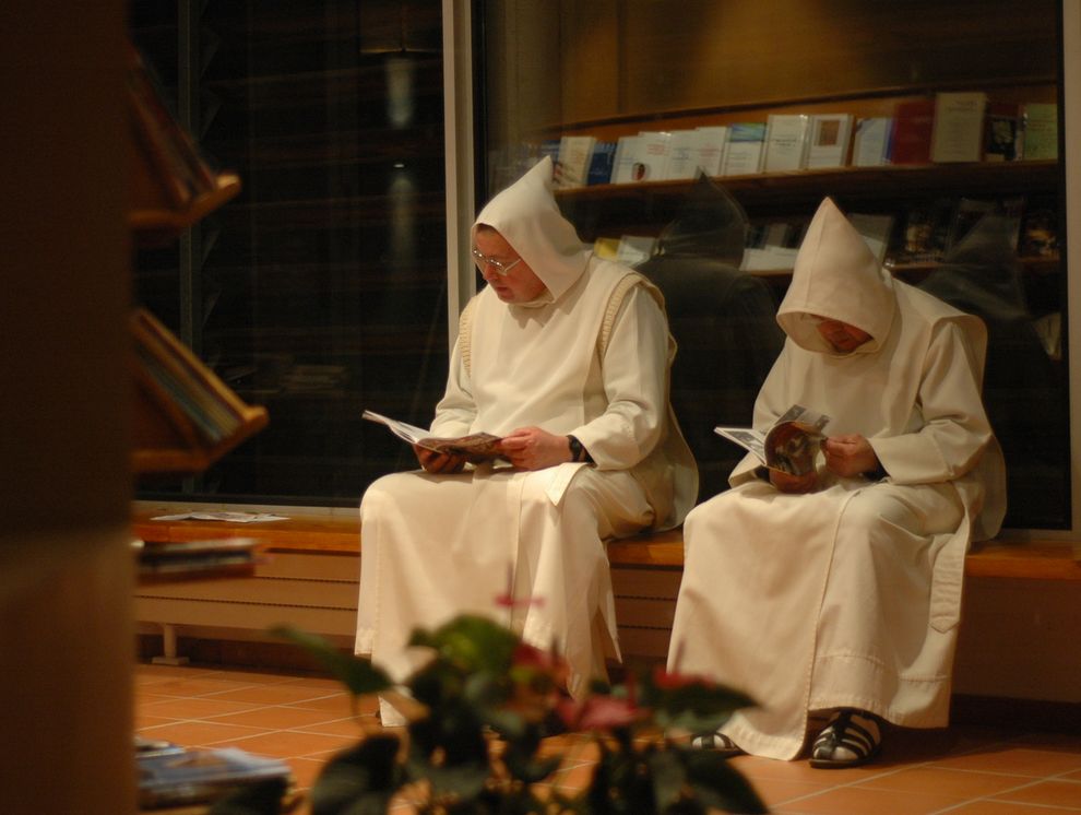 Deux moines, capuchons en tête, sont côte à côte et lisent des revues.