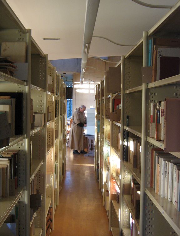 Photo prise entre deux rayons de livres. Un frère est en train de chercher une référence dans les fichiers de la bibliothèque.