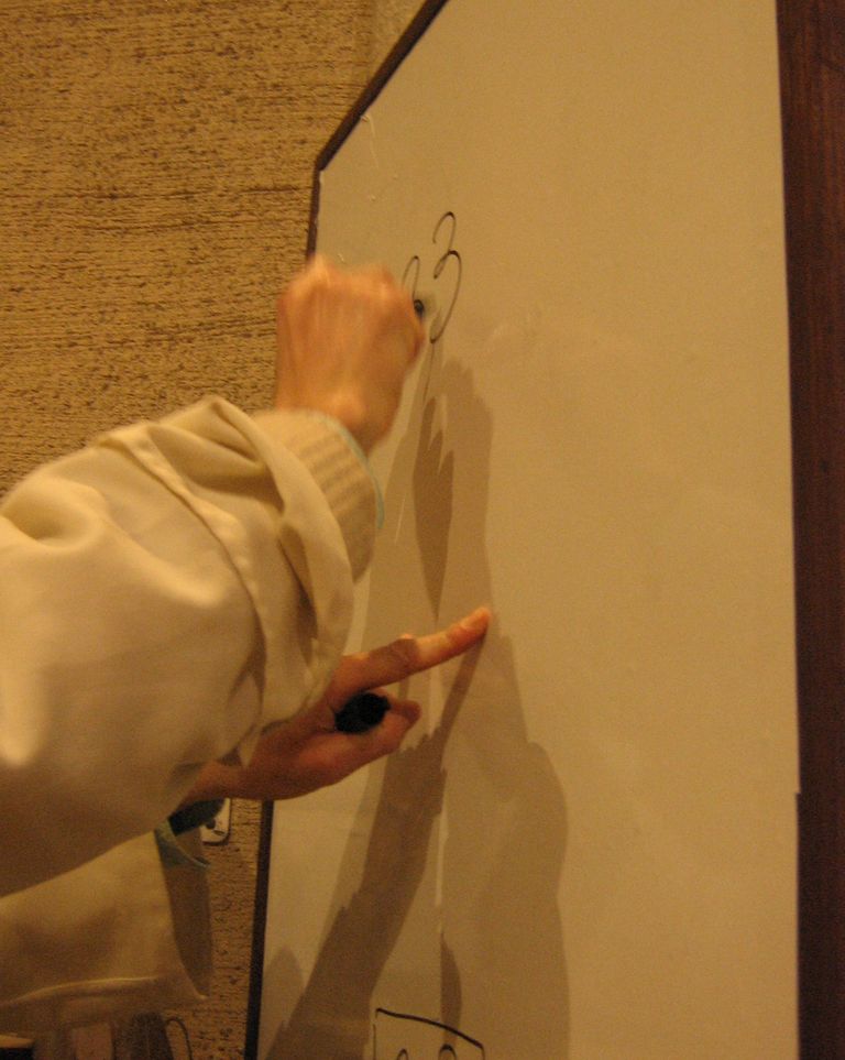 Une main de moine écrit sur un tableau blanc.