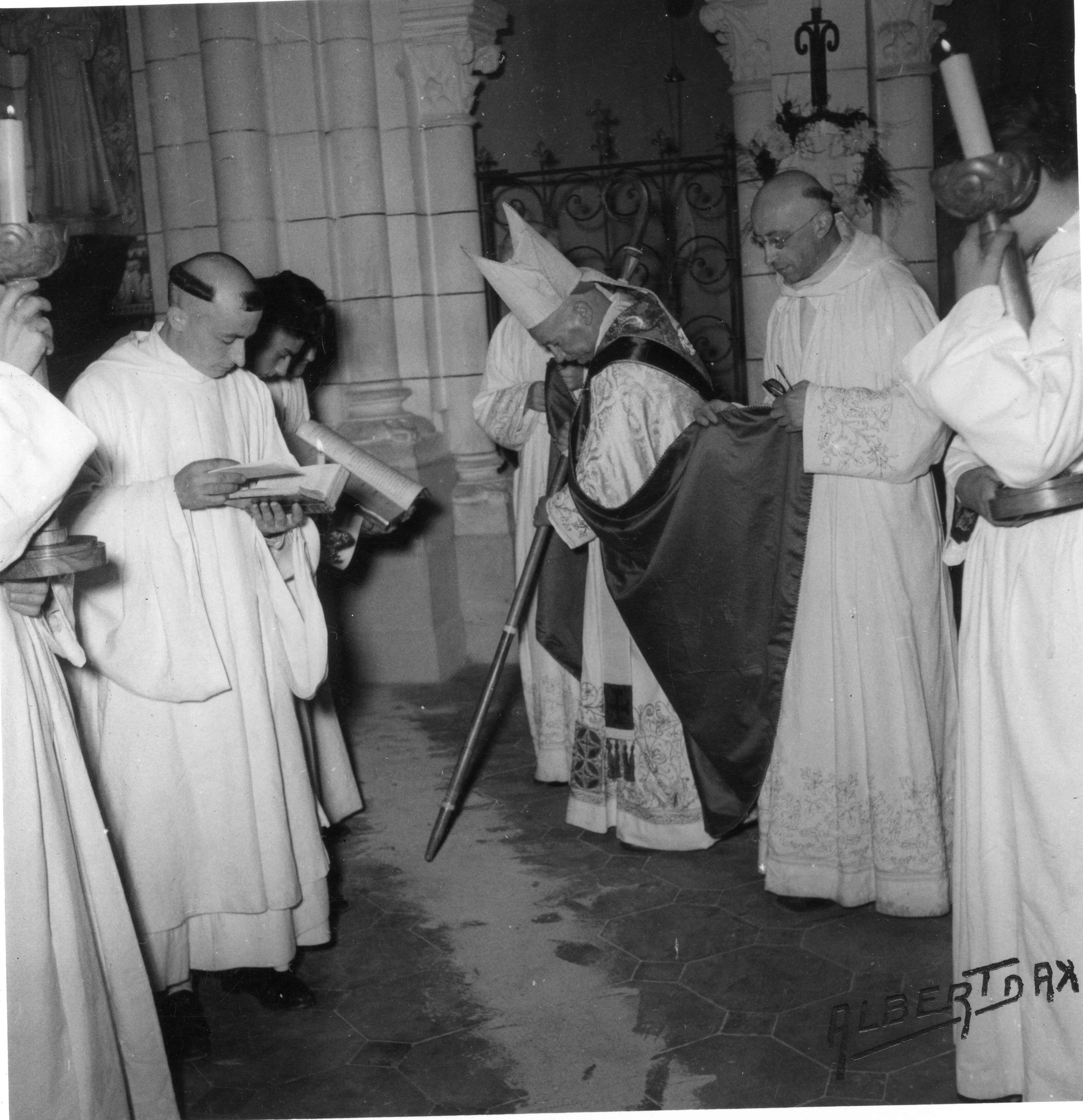 Un évêque entouré de servants trace des lettres sur le sol avec sa crosse.