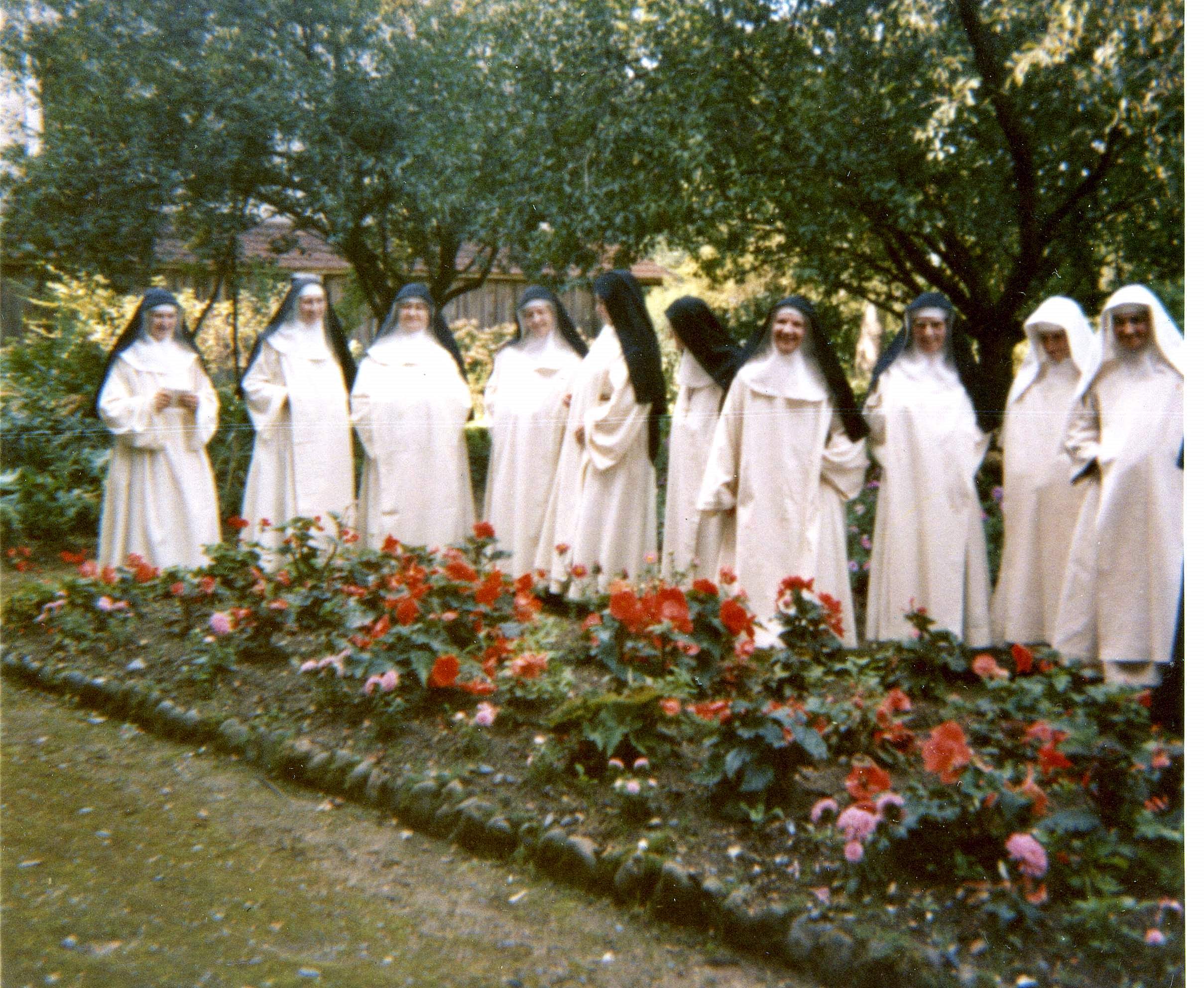 Communauté de soeurs vêtues de blanc devant une plate-bande de roses.