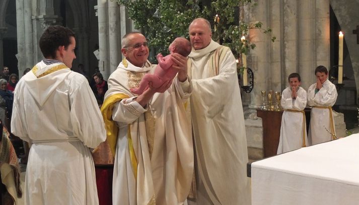 le père abbé de Maylis présente un nouveau-né qui vient d'être baptisé